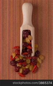 Top view of wooden scoop with mixed dried fruits against red vinyl background.
