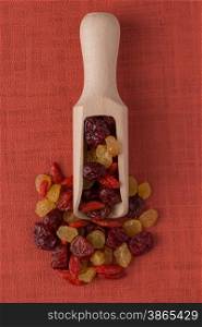Top view of wooden scoop with mixed dried fruits against red vinyl background.