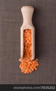 Top view of wooden scoop with peeled lentils against brown vinyl background.