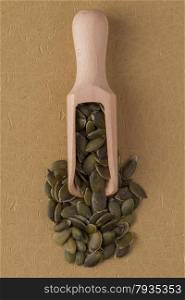 Top view of wooden scoop with pumpkin seeds against beige vinyl background.
