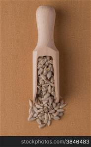 Top view of wooden scoop with shelled sunflower seeds against brown vinyl background.