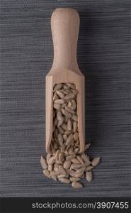 Top view of wooden scoop with shelled sunflower seeds against grey vinyl background.