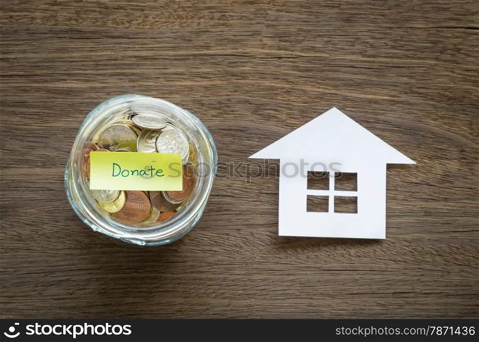 Top view of world coins in money glass jar with DONATE word label and home shape paper craft place on natural wood background