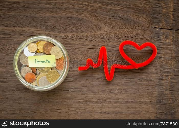 Top view of world coins in money glass jar with DONATE word label and red heart shape craft place on natural wood background
