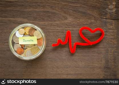 Top view of world coins in money glass jar with DONATE word label and red heart shape craft place on natural wood background