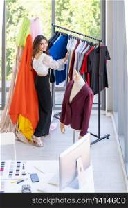 Top view of young adult asian fashion designer working from home and standing near clothing rack or clothes horse with colorful and fashionable shirts. Using for entrepreneur startup concept.