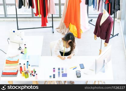 Top view of young adult fashion designer drawing and sketching her work at her atelier studio with colour palette as sole owner. Using for entrepreneur startup concept.