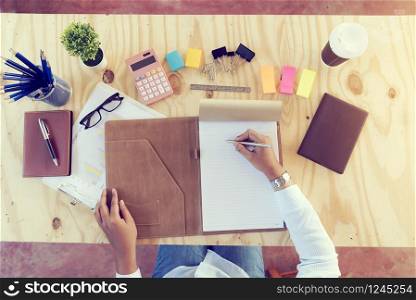 Top view of young beautiful business woman writing on her notebook at her desk with business stuff and tablet. Business Concept.