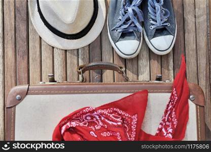 top view on a red scarf on a retro suitcase whith shoes and hat on wooden terrace