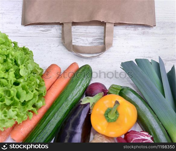 top view on a various colorful vegetables and a paper bag on a white table. fresh colorful vegetables on white table and paper bag