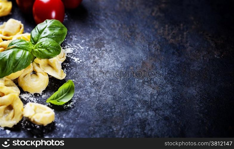 Top view on homemade pasta ravioli with flour, tomato and basil on dark vintage background