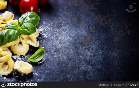 Top view on homemade pasta ravioli with flour, tomato and basil on dark vintage background