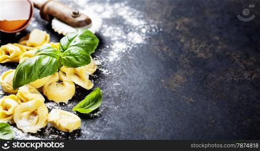 Top view on homemade tortellini with flour, tomato and basil on dark vintage background