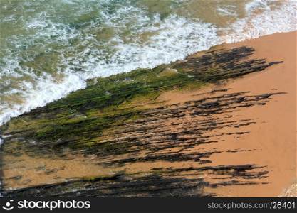 Top view on rock formations on Monte Clerigo beach and surf wave with foam (Aljezur, Algarve, Portugal).