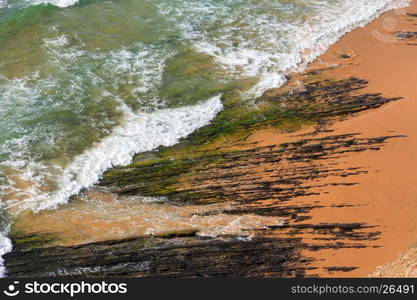 Top view on rock formations on Monte Clerigo beach and surf wave with foam (Aljezur, Algarve, Portugal).