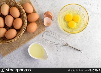 Top View organic eggs on sack cloth, many eggs on wicker basket and yolk glasses bowl, oil and egg whisk placed on the floor, preparing for cooking food or dessert, copy space