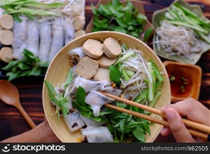 Top view people eating breakfast with Vietnamese vegetarian rolled steamed rice pancake or banh cuon with herb and sauce at home on wooden table