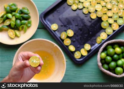 Top view people hand squeeze juice out of kumquat fruits into wooden bowl that cut in half on green peel and yellow flesh, this sour fruit rich vitamin c, healthy and make detox drink