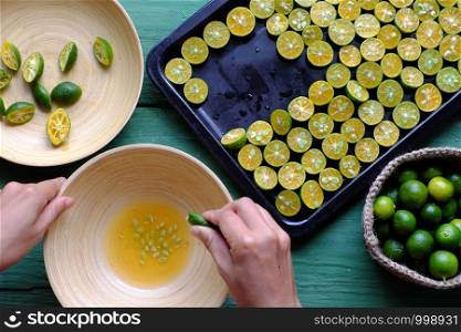 Top view people hand squeeze juice out of kumquat fruits into wooden bowl that cut in half on green peel and yellow flesh, this sour fruit rich vitamin c, healthy and make detox drink