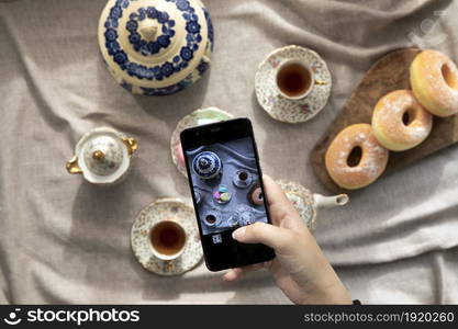 Top view picture of lady,blogger sitting in cafe and making photo with mobile of food, afternoon tea with doughnuts and macarons on the table high angle, food and social media concept close up. Top view picture of lady,blogger sitting in cafe and making photo with mobile of food, afternoon tea with doughnuts and macarons on the table high angle, food and social media concept