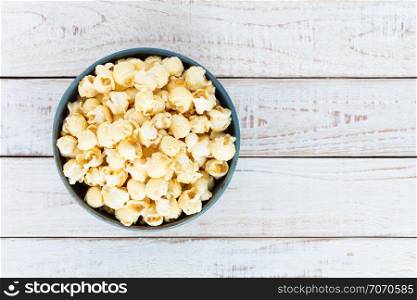 Top view popcorn in blue bowl on white wooden table.