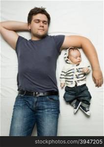 Top view portrait of stylish father and baby boy sleeping on bed
