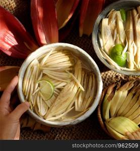 Top view prepare ingredients for vegan food from banana flower, woman hand take young bananas, soaked in lemon water, this blossom can make many vegetarian dish, healthy eating with fiber