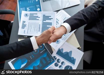 Top view professional businessman shaking hands over desk in modern office after successfully analyzing pile of dashboard data paper as teamwork and integrity handshake in workplace concept. fervent. Top view businessman handshake over desk with BI papers. fervent