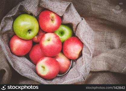 Top view red apples, green apples in basket cover with brown burlap background texture