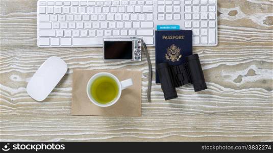 Top view shot of an old white desktop with keyboard, green tea in cup, binoculars, camera, mouse and passport in horizontal format.