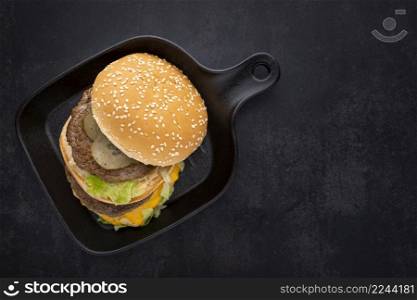 top view shot of hamburger, cheeseburger with double cutlet in black pan on the dark tone texture background with copy space for text