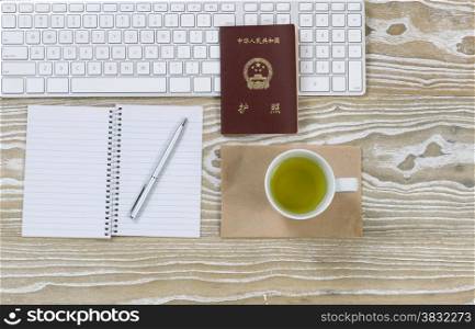 Top view shot of working desktop, China passport, keyboard and green tea drink on aged white wood surface in horizontal format.