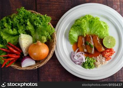 Top View Spicy salad of sardine with tomato sauce arranged nicely in white dish and ingredient herb for cooking put in a wicker basket on wooden table, copy space