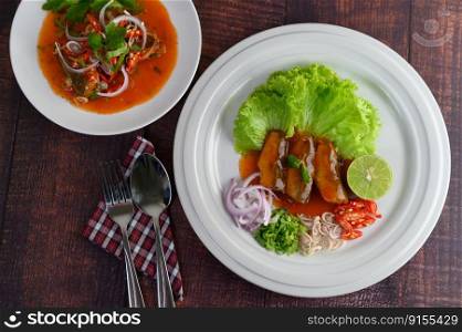 Top View Spicy salad of sardine with tomato sauce mixed with herb and arranged nicely in white dish and sparken stainless spoon and fork over napkin on wooden table, copy space
