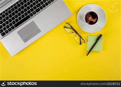 Top view studio photo of a laptop, a cup of coffee and stationary elements on a yellow background. Top view studio photo of a laptop, a cup of coffee and stationary elements