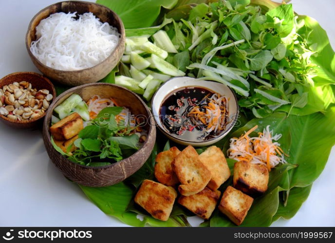 Top view vegan food ready to eat on leaf background, fried tofu, bun, cucumber and herbal leaf as mint, lettuce with soy sauce, healthy eating with vegetable make for good natural immunity