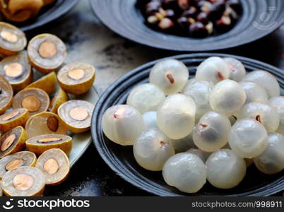 Top view Vietnamese tropical sweet, watery pulp fruit, close up Longan fruits flesh in translucent white on black plate with black seed, yellow peel, cut in half of dragon eye fruits background