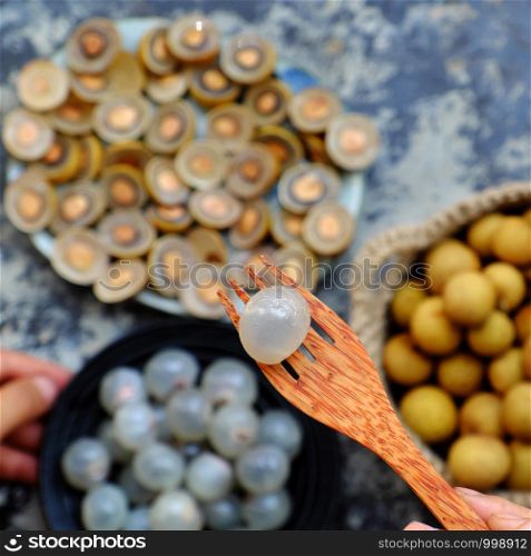 Top view Vietnamese tropical sweet, watery pulp fruit, close up Longan fruits flesh in translucent white on black plate with black seed, yellow peel, cut in half of dragon eye fruits background