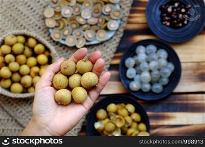 Top view Vietnamese tropical sweet, watery pulp fruit, close up Longan fruits in people hand with flesh in translucent white black seed, yellow peel, cut in half of dragon eye fruits background
