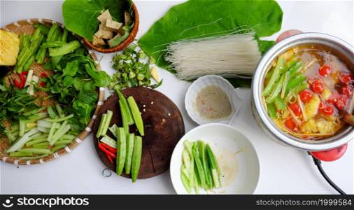 Top view Vietnamese vegan food, healthy eating from vegetal, green vegetables hot pot homemade from tomato, okra, dragon bean, herbal leaf, spinach, tofu skin, and dried noodles