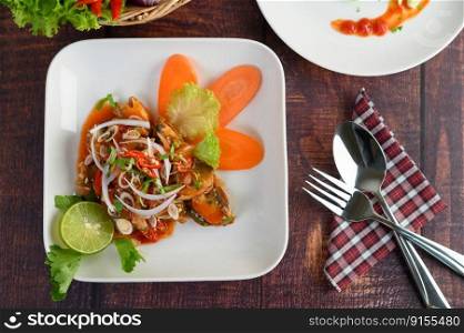 Top View with Spicy salad of sardine in tomato sauce mixed with herb is beautifully arranged in the shape of fish and stainless spoon and fork on napkin nearly on wooden table
