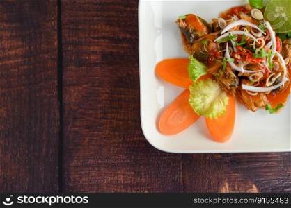 Top View with Spicy salad of sardine in tomato sauce mixed with herb is beautifully arranged in the shape of fish in white plate on wooden table, copy space