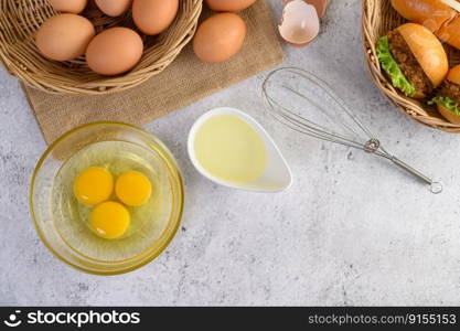Top view with yolk in glass bowl and in wicker basket, hambur≥rs and hotdog with slice tomato and≤ttuce in weave basket, oil in cup and egg whisk placed≠arly