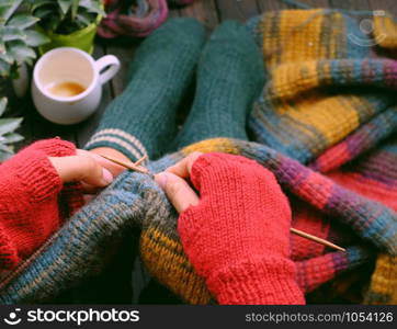 Top view woman feet with socks, sitting at home balcony, hand with knitted gloves hold knitting needle to knit colorful wool scarf for meaningful handmade winter gift when wintertime come.