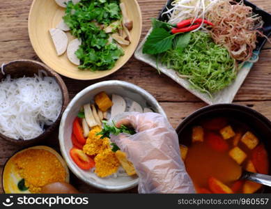 Top view woman hand prepare homemade breakfast, vegan rieu noodle soup or vegetarian crab paste vermicelli soup, a traditional Vietnamese dish, plate of vegetables, herbs, soup pot, ready to eat