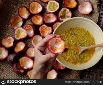 Top view woman hand processing passion fruit by cut in half Passiflora edulis, with a spoon people take soft pulp and seeds inside a hard rind to bowl