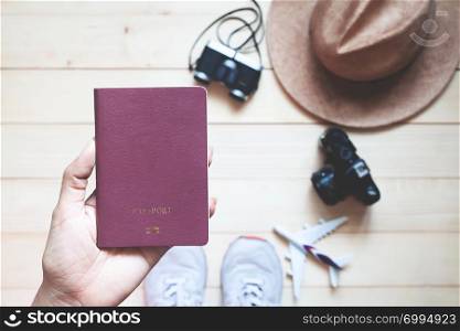 Top view woman holding passport book with cameras and hat on wooden floor. Travel lifestyle concept