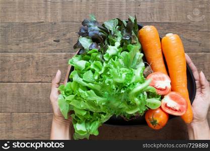 Top view woman's hands holding a plate of fresh vegetables