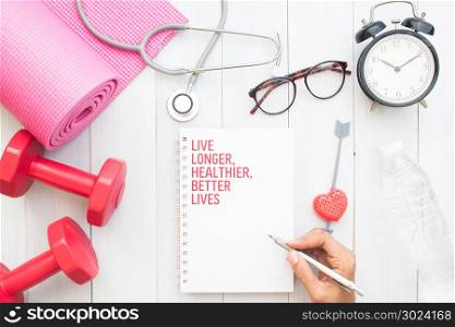 Top view woman writing on notebook and sport equipments on white wooden table, Healthcare and Fitness concept