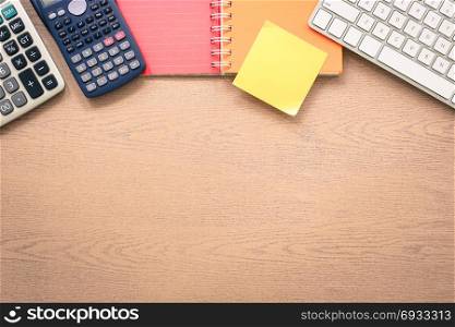 Top view wooden office table with blank desk space. Color paper book, keyboard, calculator and yellow sticky note on top side. Mockup background for announcement concept, vintage and retro styles.